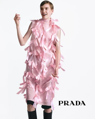 Model in pink ribbon dress wearing black boots standing against a white backdrop