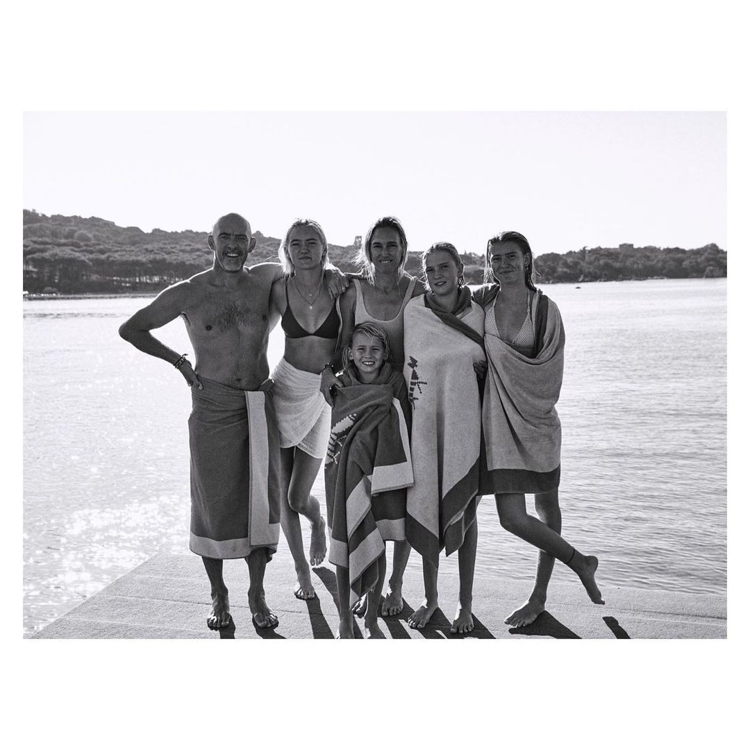 Black and white shot of a group of six people, including adults and a child, standing on a dock near a body of water.