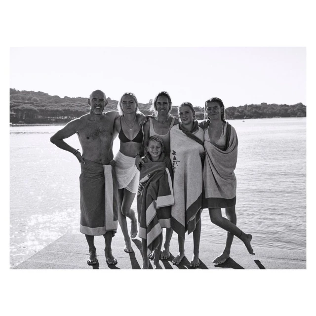 Black and white shot of a group of six people, including adults and a child, standing on a dock near a body of water.