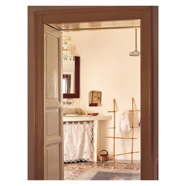Bathroom interior with a vanity, decorative mirror, chandelier, and bamboo ladder seen through a doorway with detailed tile flooring.
