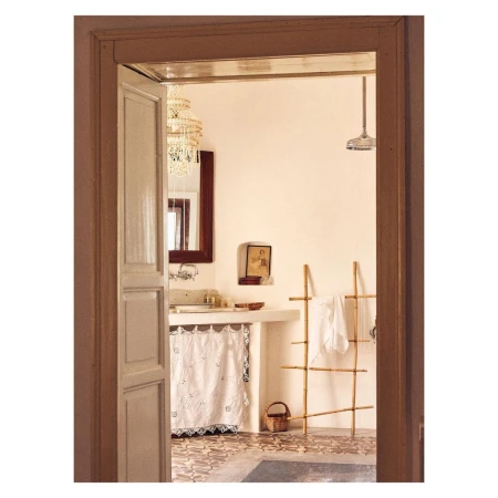 Bathroom interior with a vanity, decorative mirror, chandelier, and bamboo ladder seen through a doorway with detailed tile flooring.