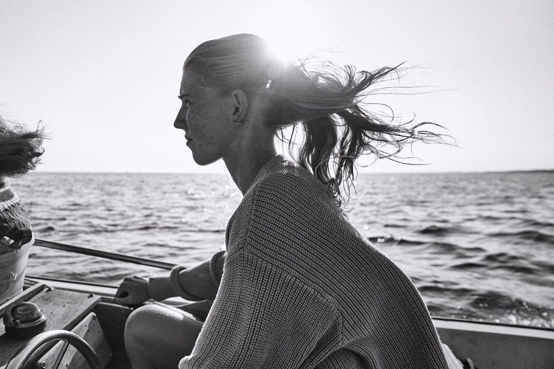 Profile of a young woman sailing on a boat, with sunlit water in the background in a black and white outdoor shot.