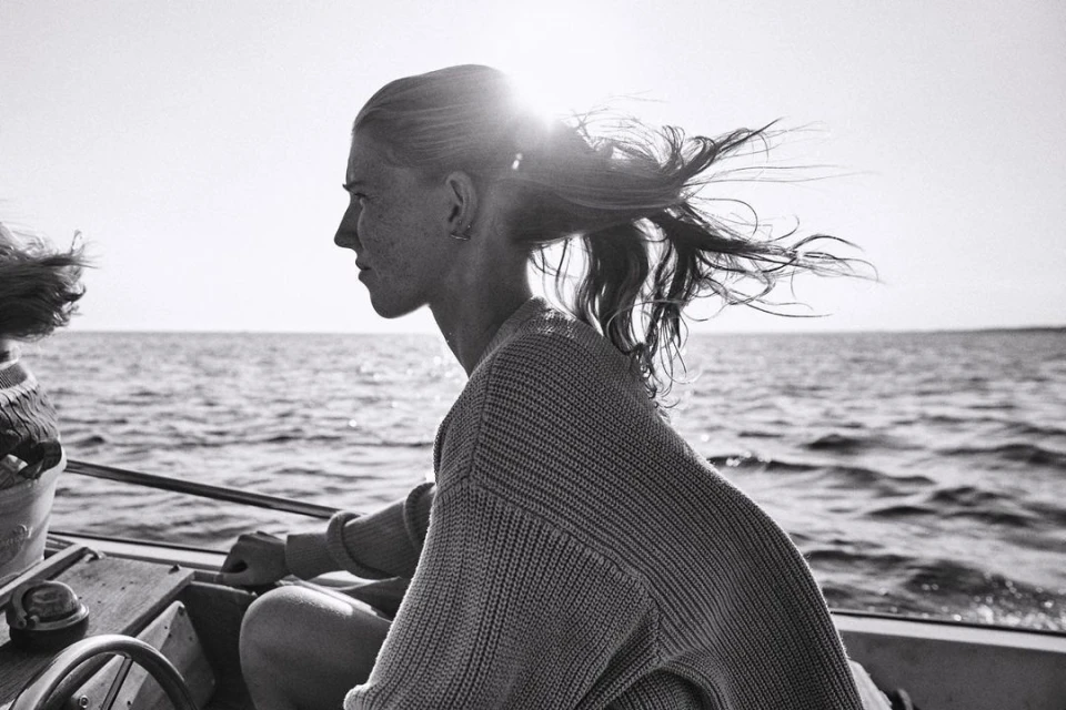 Profile of a young woman sailing on a boat, with sunlit water in the background in a black and white outdoor shot.