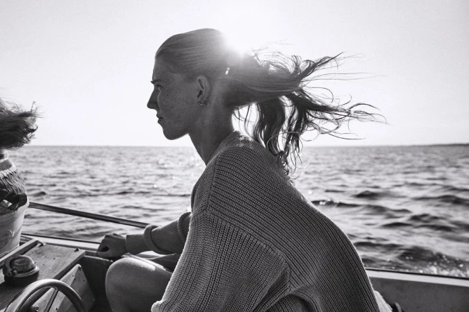 Profile of a young woman sailing on a boat, with sunlit water in the background in a black and white outdoor shot.
