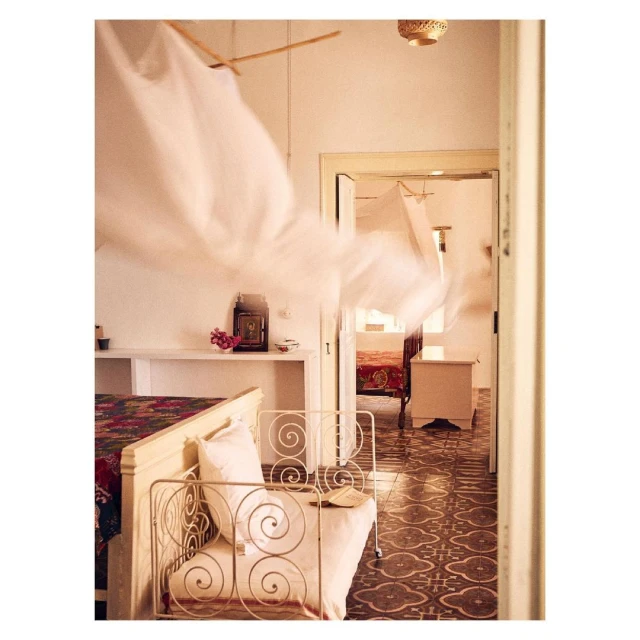Interior view of a bedroom with a white bed, patterned tile floor, and sheer white fabric draped from the ceiling.