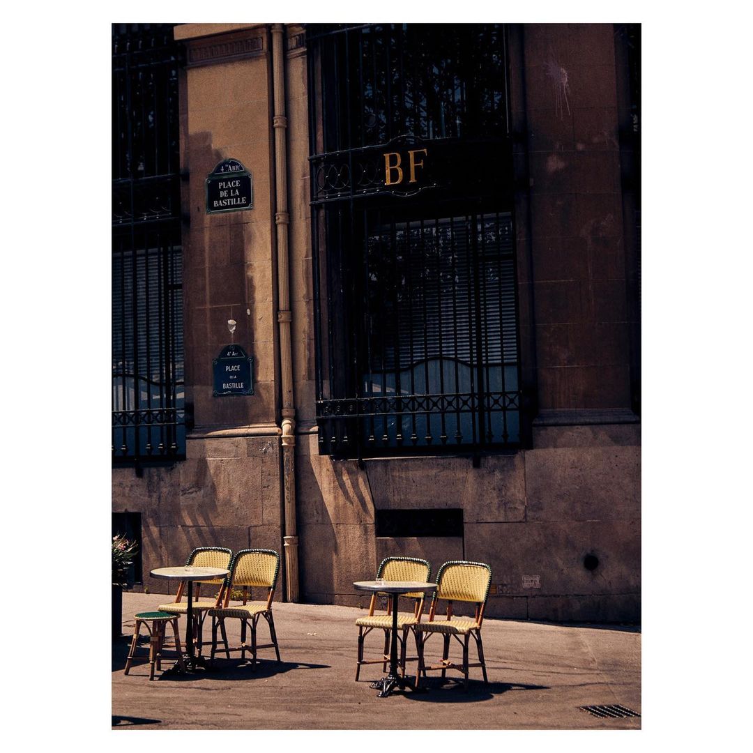 Outdoor cafe setting in Paris, featuring empty tables and chairs outside a building with classic French architectural details.