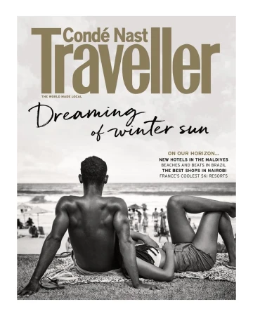 Condé Nast Traveller cover: a back view of a man and a woman lying on the beach, with the ocean and other beachgoers behind them.