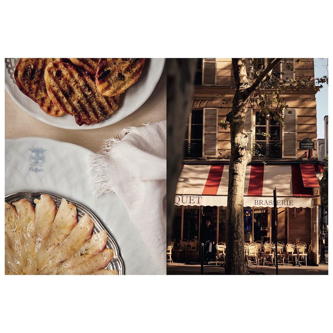 Grilled bread and sliced fish served on plates, beside a brasserie facade with outdoor seating and a red and white striped awning.