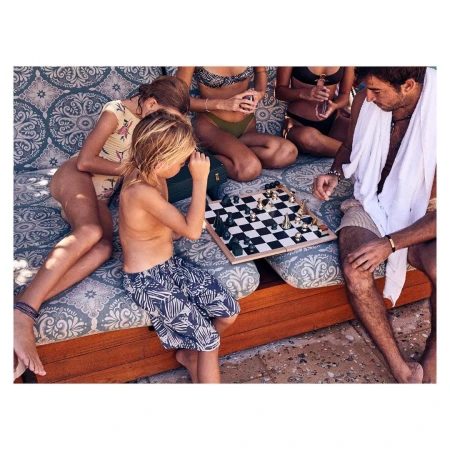 Leisure scene features a boy and group playing chess outdoors on a patterned daybed, evoking relaxation and a vacation atmosphere.