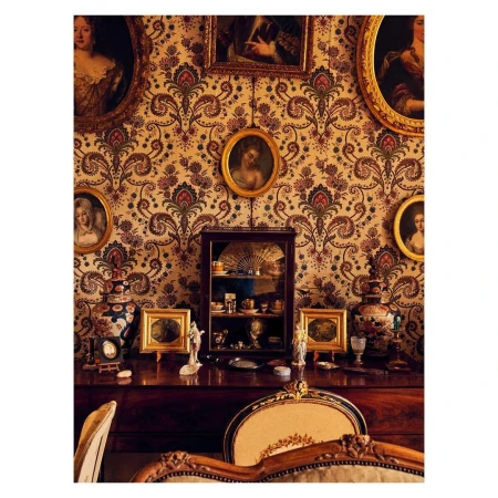 Vintage interior with ornate wallpaper, framed portraits, display cabinet, and decorative objects on a wooden dresser with chair detail.