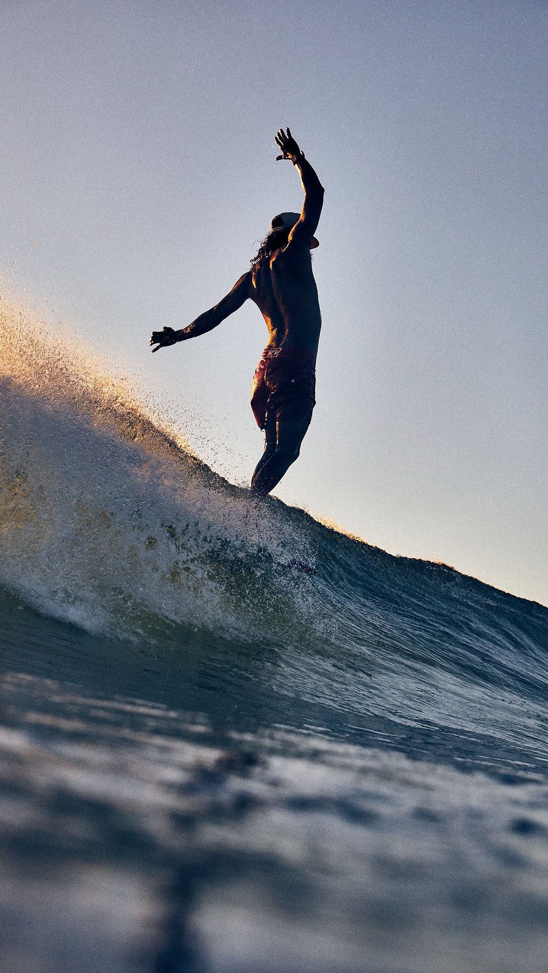 Silhouette of a person surfing on a wave at sunset, captured from a low angle, emphasizing the sport and the ocean's power.
