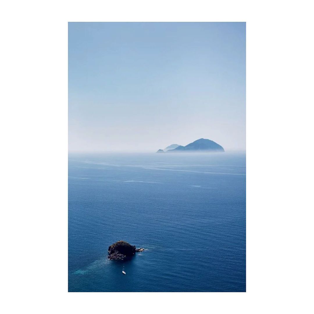 Scenic view of deep blue ocean with small islands under a clear, pale blue sky. Tranquil seascape showcases natural beauty.