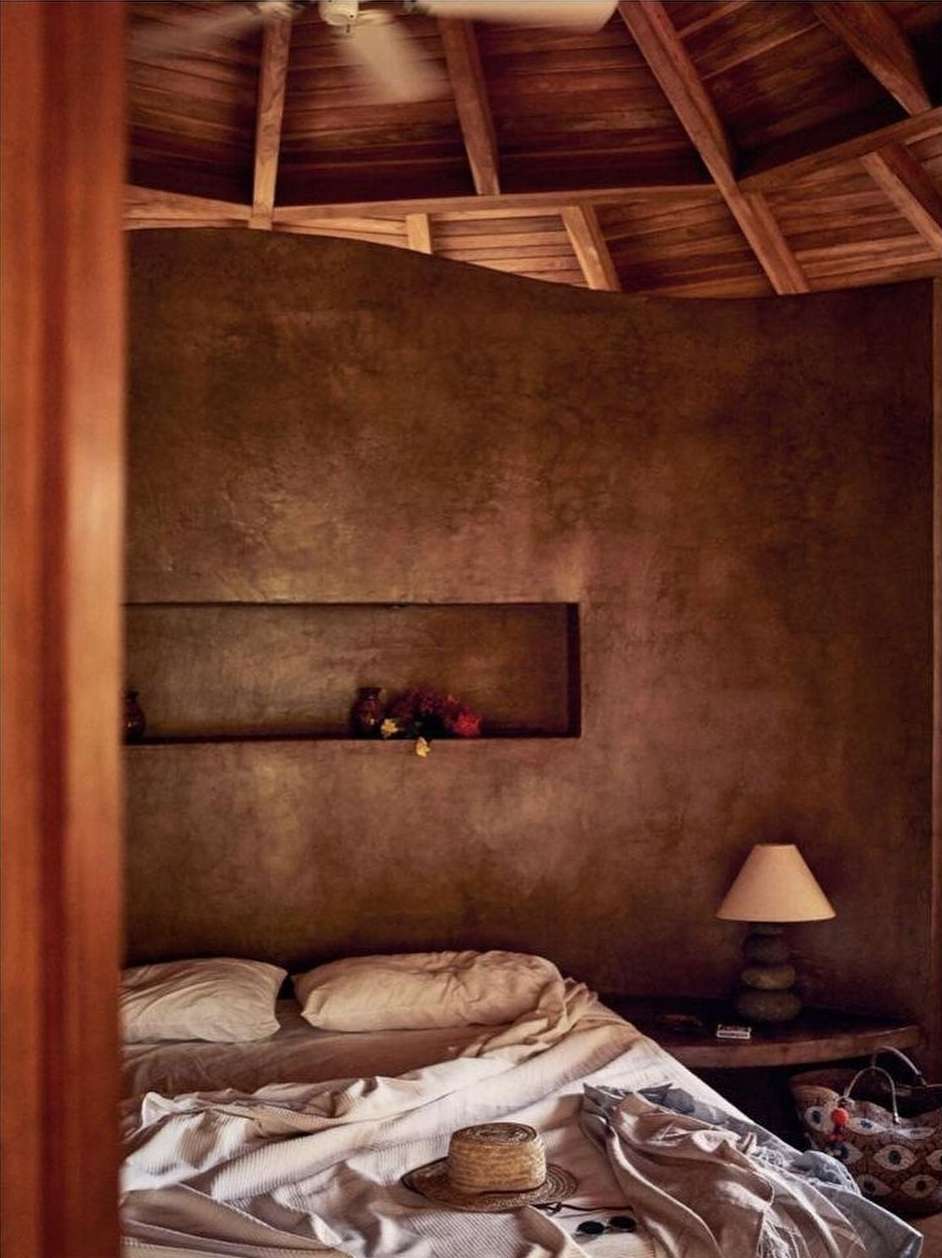 Bedroom interior featuring a made bed with white linens, straw hat, and sunglasses, set against a rustic brown wall and wood ceiling.