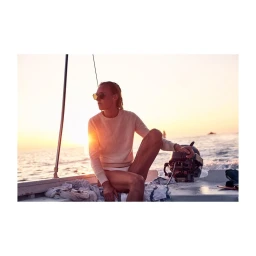 Woman wearing sunglasses and a knitted sweater seated on a small motorboat at sunset