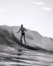 Black and white photograph of a woman surfing on a wave, captured by Oliver Pilcher in New York.