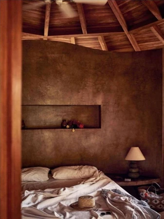 Interior bedroom view featuring a made bed with white linens, textured brown walls, and a wooden ceiling.