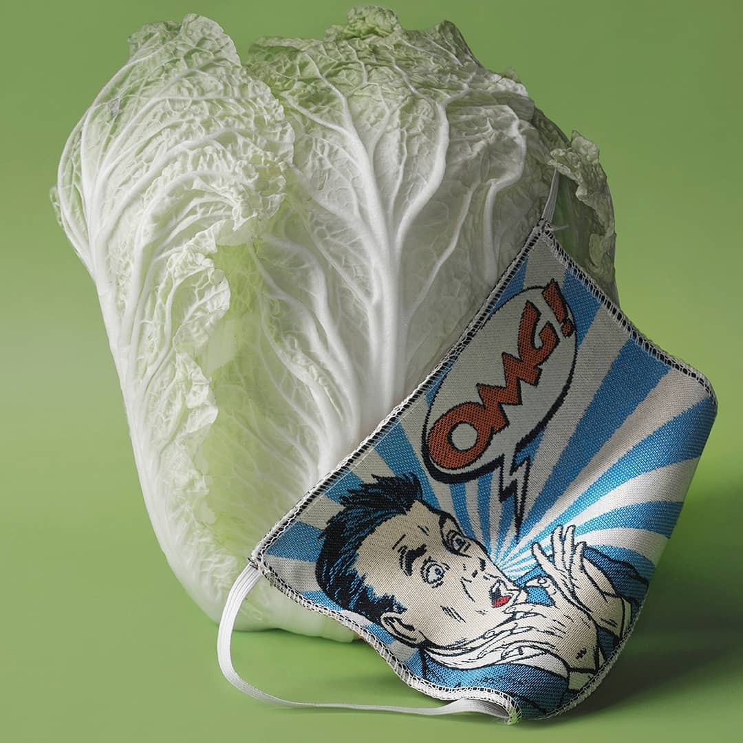 Still life featuring napa cabbage alongside a reusable face mask with an illustration of a surprised man and the word 'OMG!'