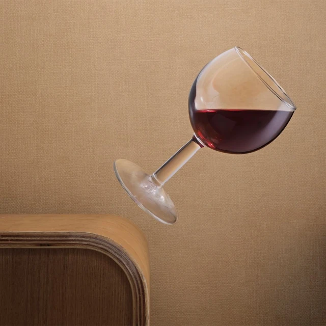 Floating red wine in a clear glass, gracefully angled above a wooden table against a textured beige background creating a serene ambiance.