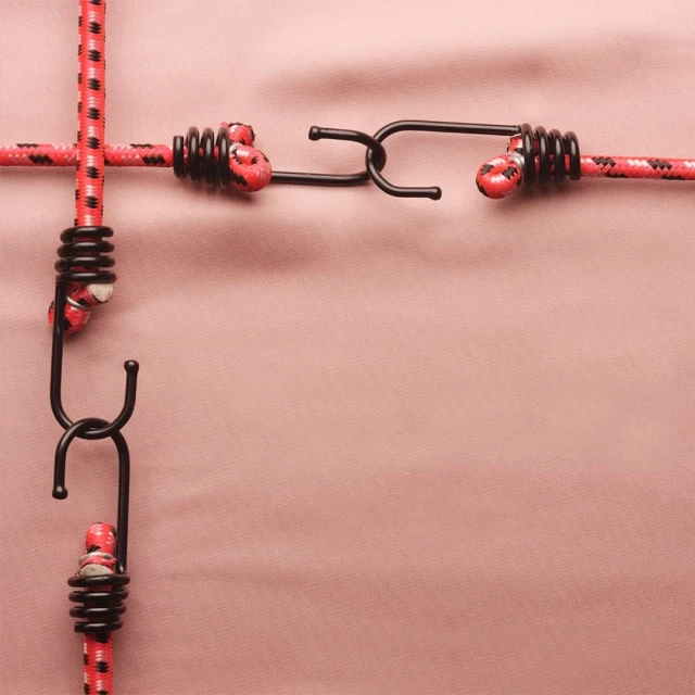 Close-up shot of red and black bungee cords interwoven on a light pink background, creating a crisscross pattern and a modern look.