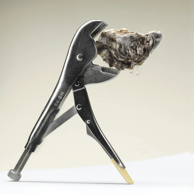 Close-up studio shot of a silver metal locking plier tool holding an oyster against a creamy background, creating a stark contrast.
