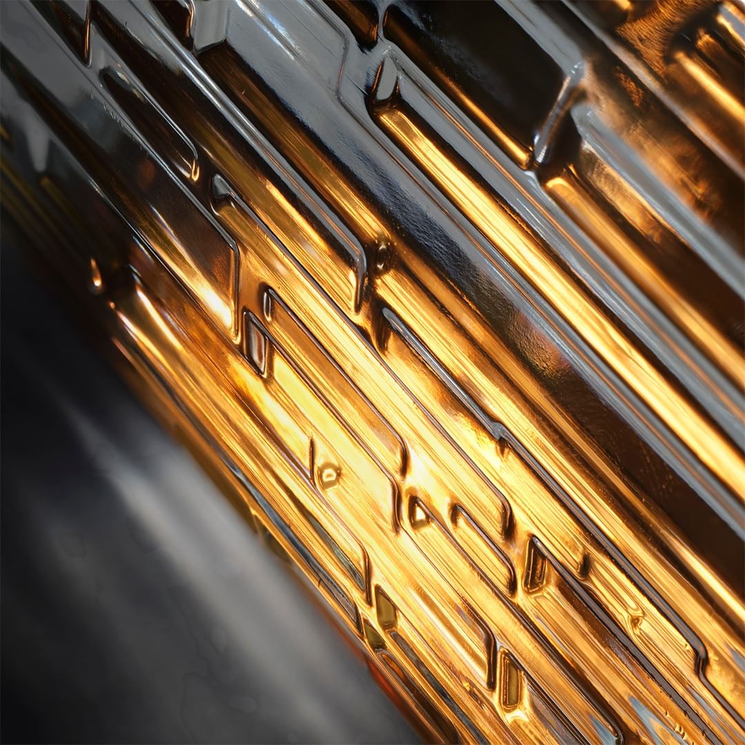 Close-up abstract photograph of a glossy surface with parallel, raised diagonal lines, reflecting warm, golden light, and dark, contrasting shadows.