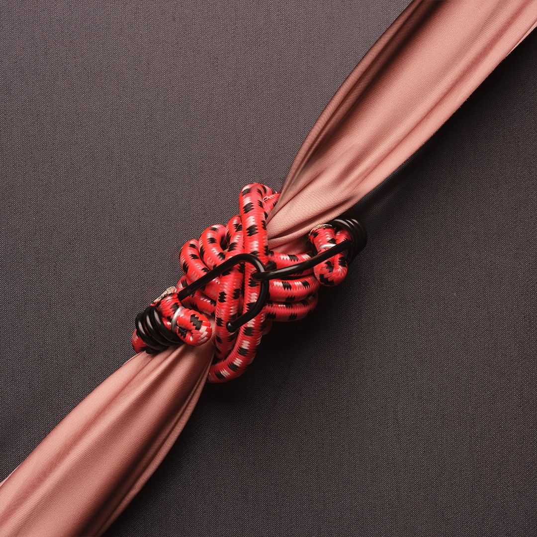 Close-up of a red bungee cord secured to a beige fabric, set against a dark grey background, emphasizing texture and color contrast.