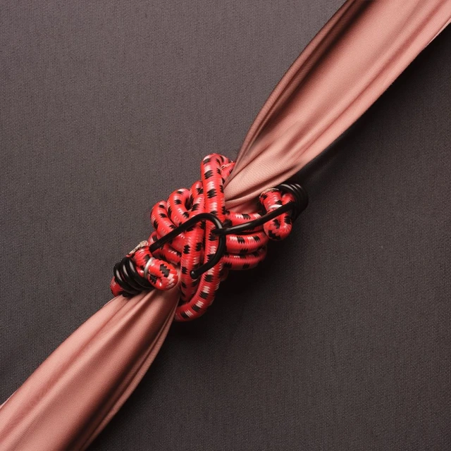 Close-up of a red bungee cord secured to a beige fabric, set against a dark grey background, emphasizing texture and color contrast.