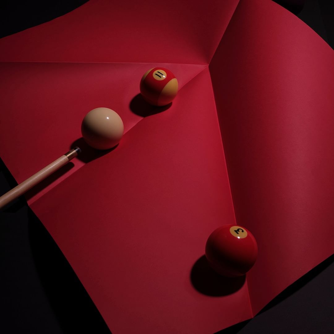 Still life photo of billiard balls on folded red paper. One white and two red balls with the numbers 3 and 11 are visible.