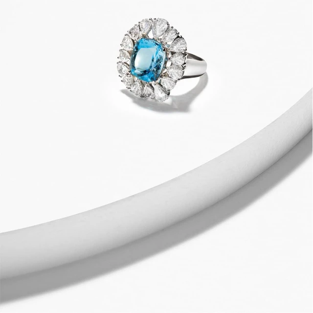 Elegant silver ring featuring a large, light blue gemstone surrounded by small white gemstones, isolated on a white surface.