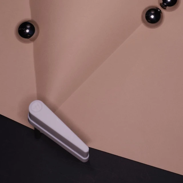 Still life of gray spheres on a peach surface with a white lever extending to a black surface on the bottom left, creating graphic art.