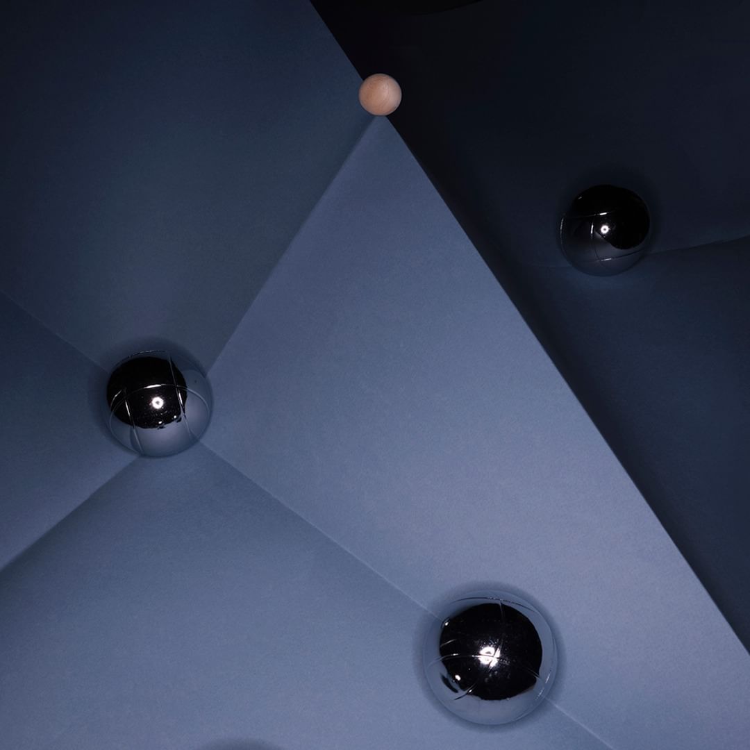 Geometric shapes in shades of blue with shiny silver and wooden spheres create an abstract, minimalist composition with stark contrasts.