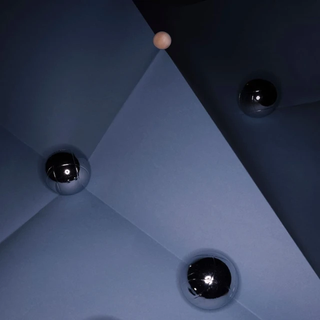Geometric shapes in shades of blue with shiny silver and wooden spheres create an abstract, minimalist composition with stark contrasts.