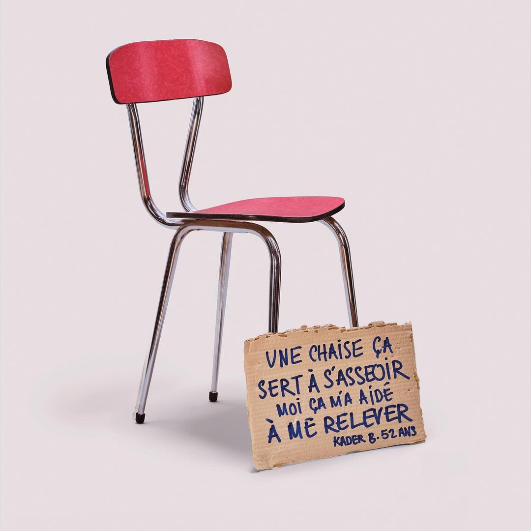 Red chair with chrome legs and cardboard sign with French text in a photo studio setting. Simple chair design, clean background.