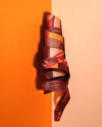 A rolled patterned fabric strip featuring geometric shapes against a split orange and peach backdrop by Olivier Foulon