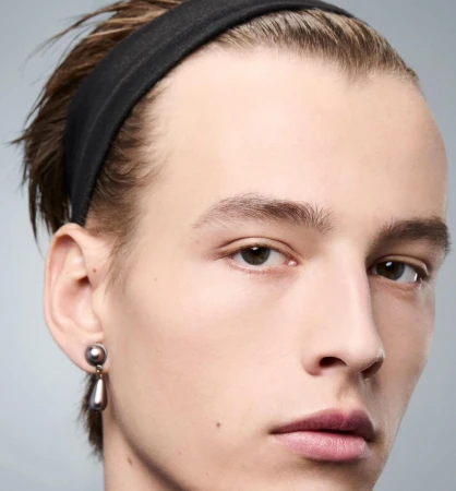 Close-up studio portrait of a young adult male with neutral expression wearing a black headband and a tear-drop earring.