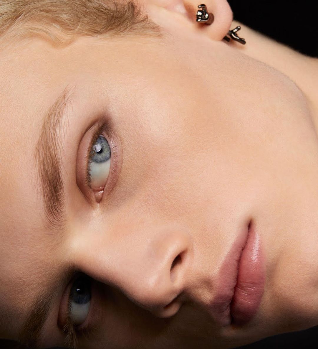 Close-up studio portrait of an adult woman with light skin and short blonde hair, featuring distinctive earrings and soft, diffused lighting.