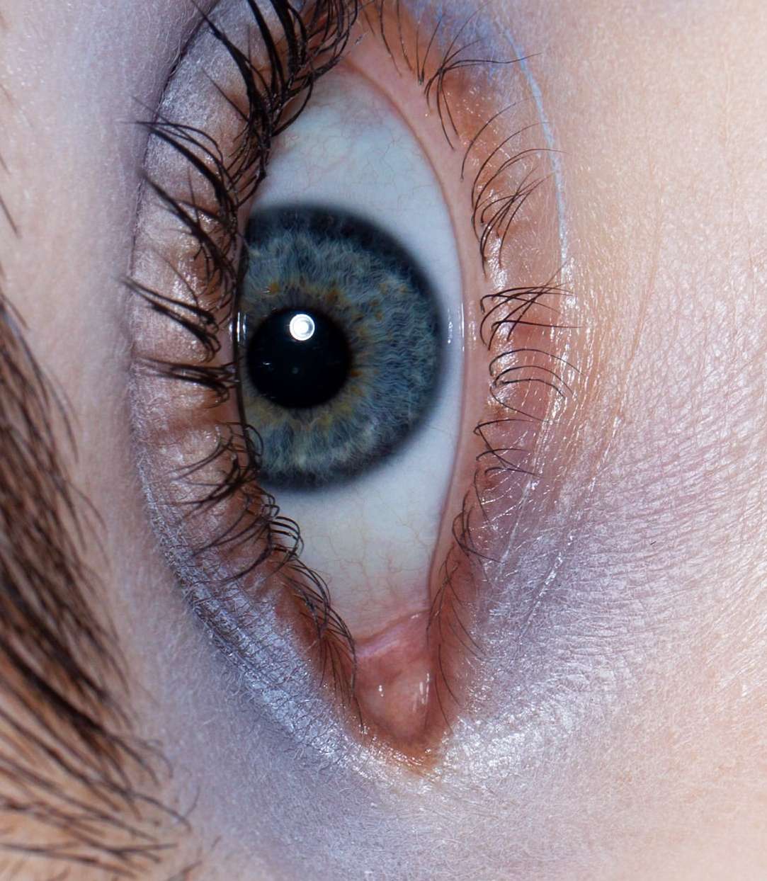 Macro shot of a blue human eye with dark lashes and makeup around the eye area, photographed in a portrait orientation.