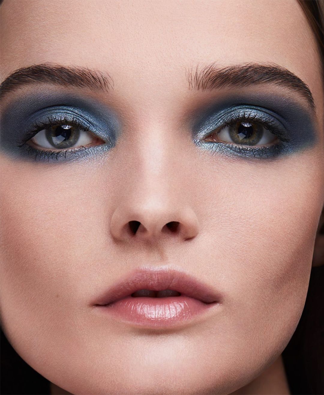 Close-up beauty portrait of a woman with dramatic blue eyeshadow and glossy nude lips photographed by Olivier Rose.