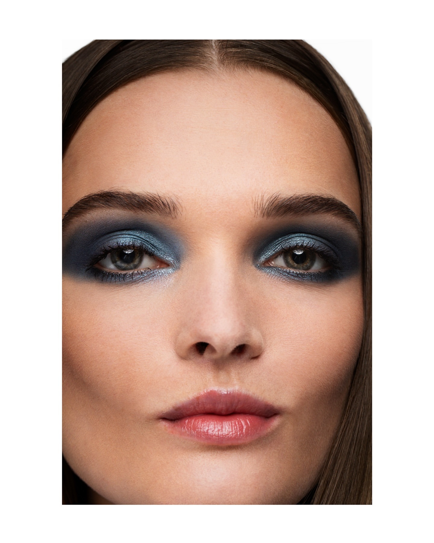 Close-up of a woman's face with dramatic blue eyeshadow, smooth skin, and glossy lips in a beauty shot for makeup trends.