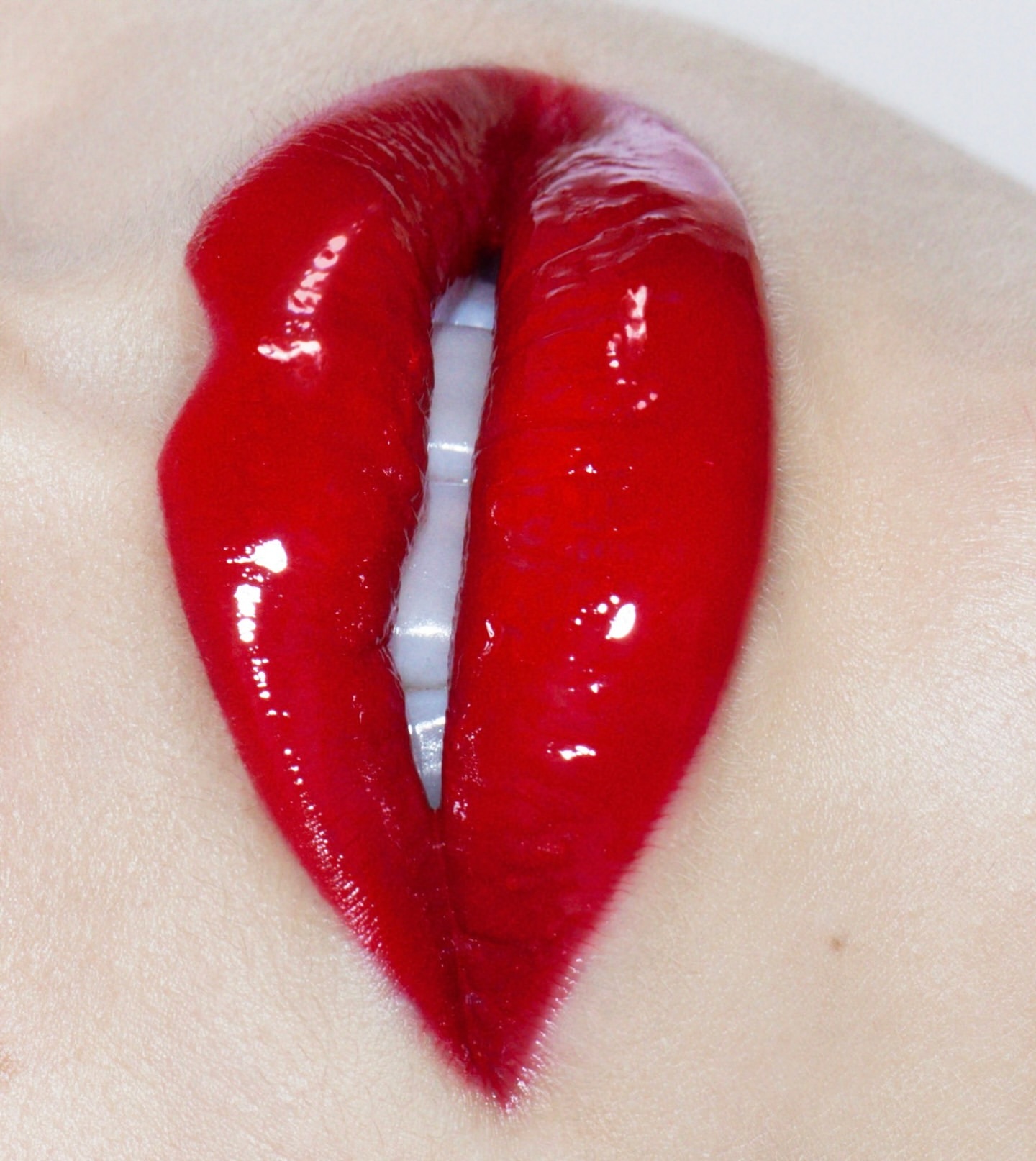 Close-up studio shot of red glossy lips with visible teeth, conveying beauty and cosmetic appeal against a neutral skin background.
