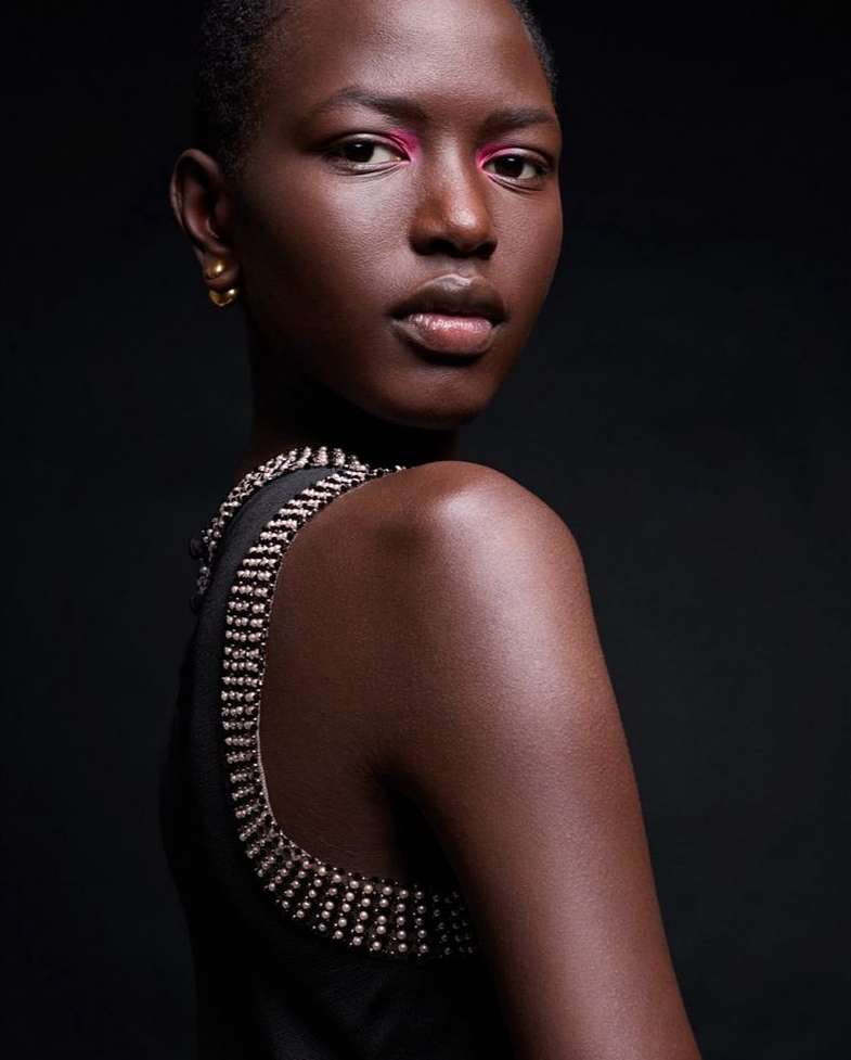 Portrait of a woman with dark skin and short hair looking over her shoulder. She is wearing a black top with a jeweled neckline.