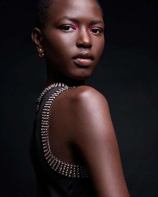 Portrait of a woman with dark skin and short hair looking over her shoulder. She is wearing a black top with a jeweled neckline.