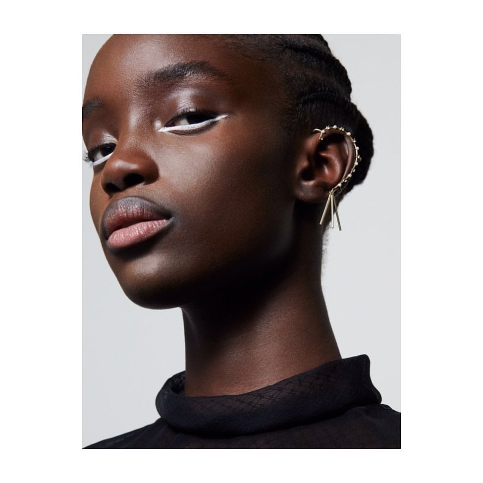 Close-up studio shot of an African-American woman with strong white eyeliner, gold ear jewelry, and a black high-neck top.