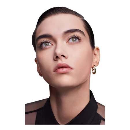 Close-up portrait of a woman looking upward, wearing a black top and gold hoop earrings against a white background.