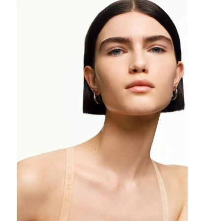 Close-up portrait of a woman with dark short bob hair and silver hoop earrings against a white background