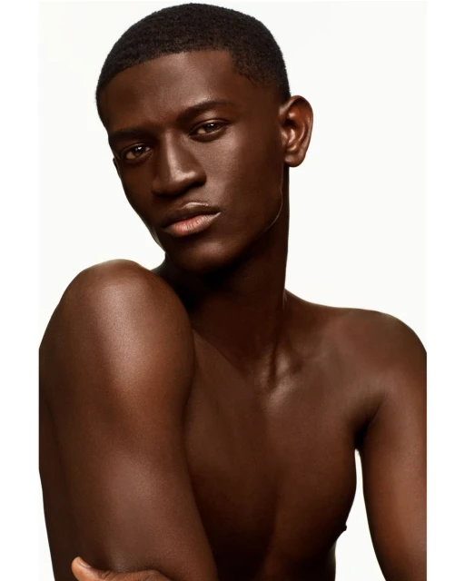 Portrait of a dark-skinned young adult male with a serious expression, clean haircut, and bare upper body against a clean white background.