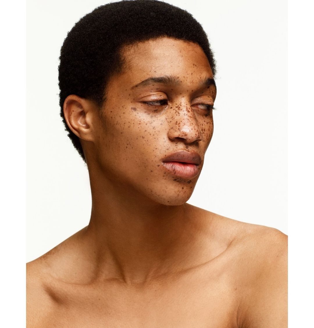 Portrait of a young adult male with freckles against a white background, showcasing his bare chest, dark hair, and skin details.