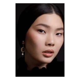 Close-up portrait of an East Asian woman wearing statement drop earrings and a black top against a dark background by Olivier Rose