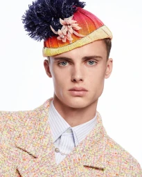 Portrait of a man wearing a colourful knitted beanie with a large dark pom-pom and a textured tweed jacket by Olivier Rose.