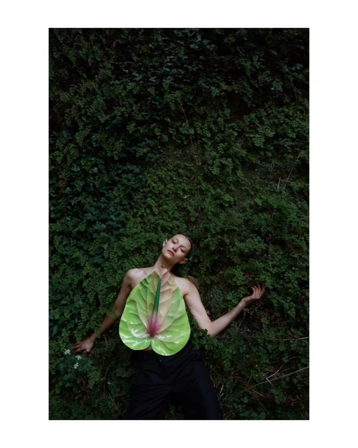 Woman laying in ferns wearing anthurium flower. Anthurium flower covers model's chest, ferns are in the background, dark and moody.